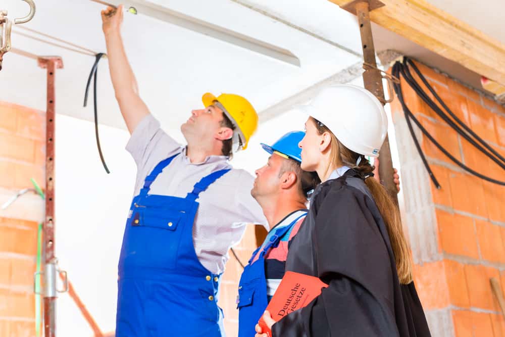 Reviewer or expert or lawyer and builder or worker with helmets controlling a construction or building site to report defect or fault or deficiency in a protocol